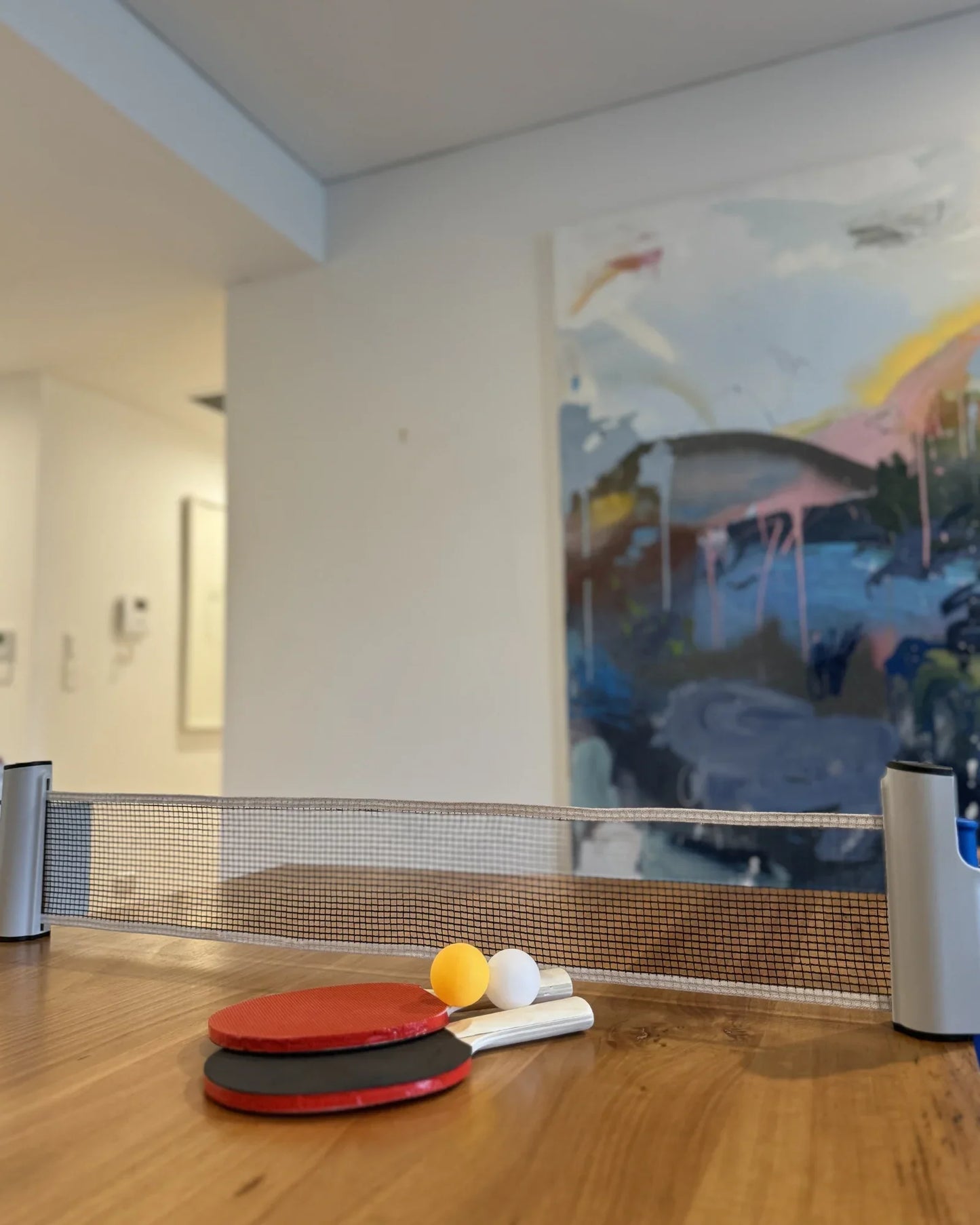 Jogo de tênis de mesa portátil com rede, duas raquetes e duas bolas sobre mesa de madeira