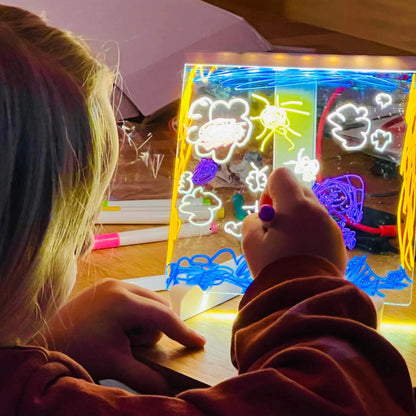 Criança desenhando em lousa de LED para colorir, com marcadores coloridos, brinquedo educativo.