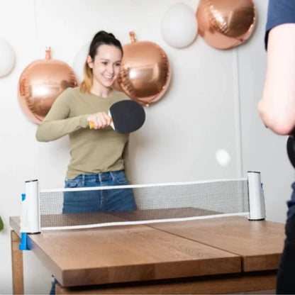 Jovens jogando tênis de mesa com rede retrátil em mesa de madeira, ambiente decorado.