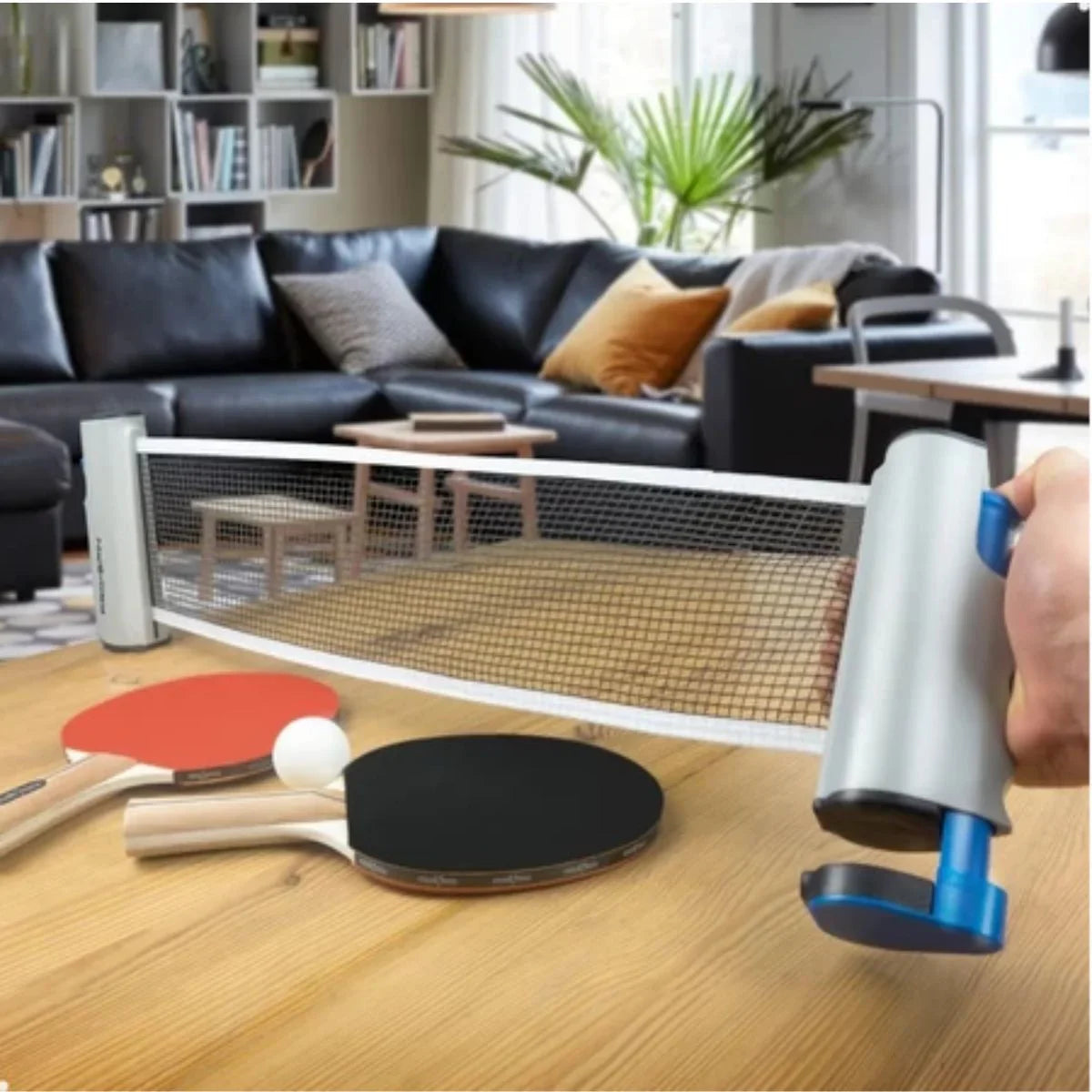 Rede retrátil de tênis de mesa instalada em mesa, raquetes e bola de ping pong em destaque em sala de estar.